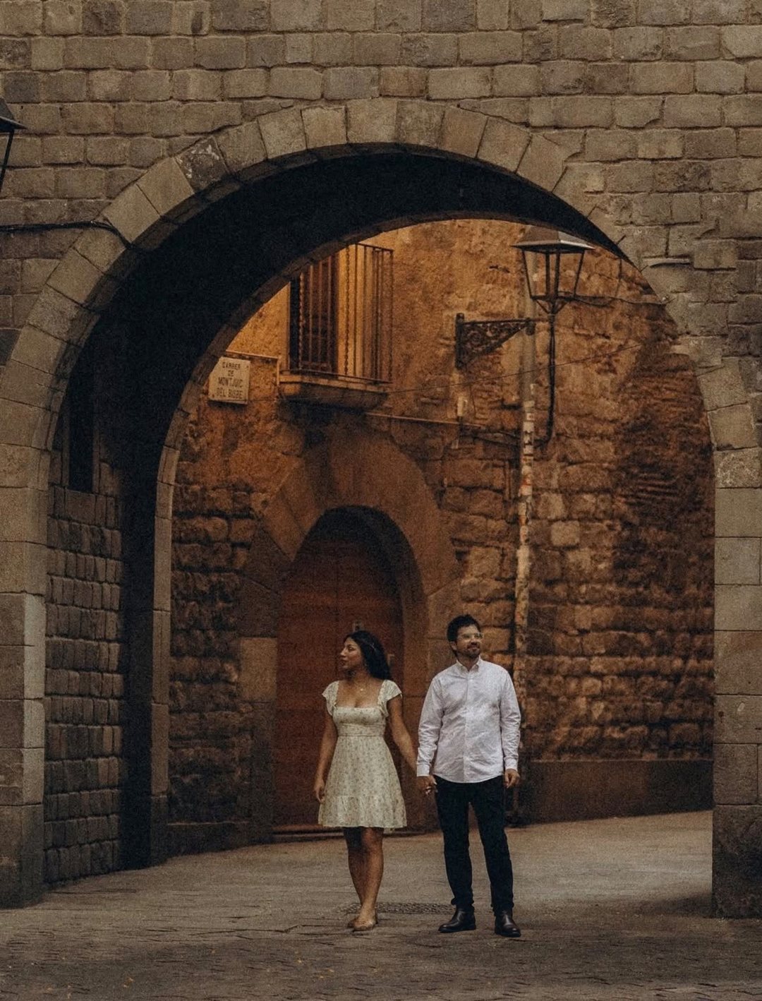 David y Banellye tomados de la mano bajo un arco de piedra en Barcelona